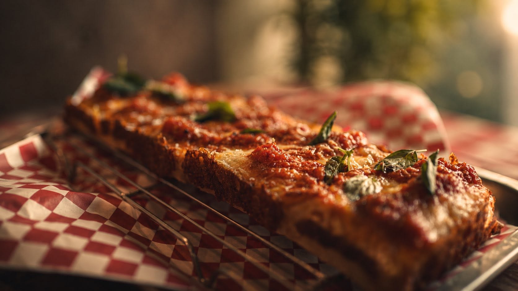 Detroit-style pizza glowing in warm window light on red checkered paper